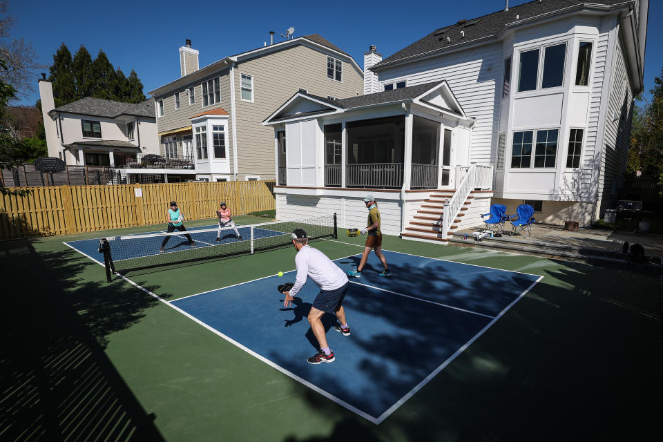 Four players playing pickleball on a backyard court.