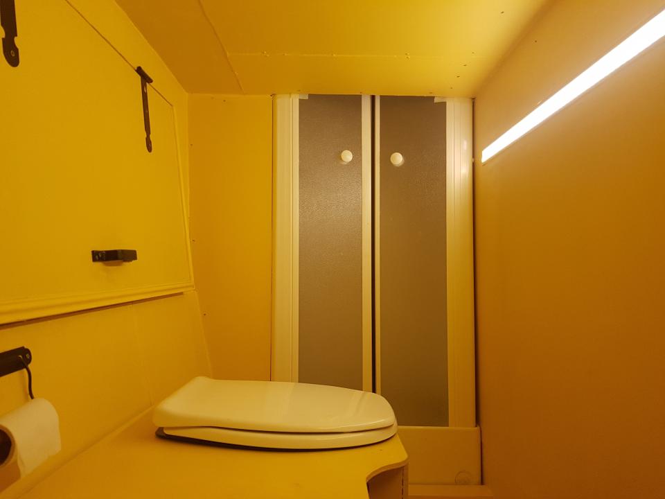 The yellow bathroom aboard the double decker bus with a toilet and shower