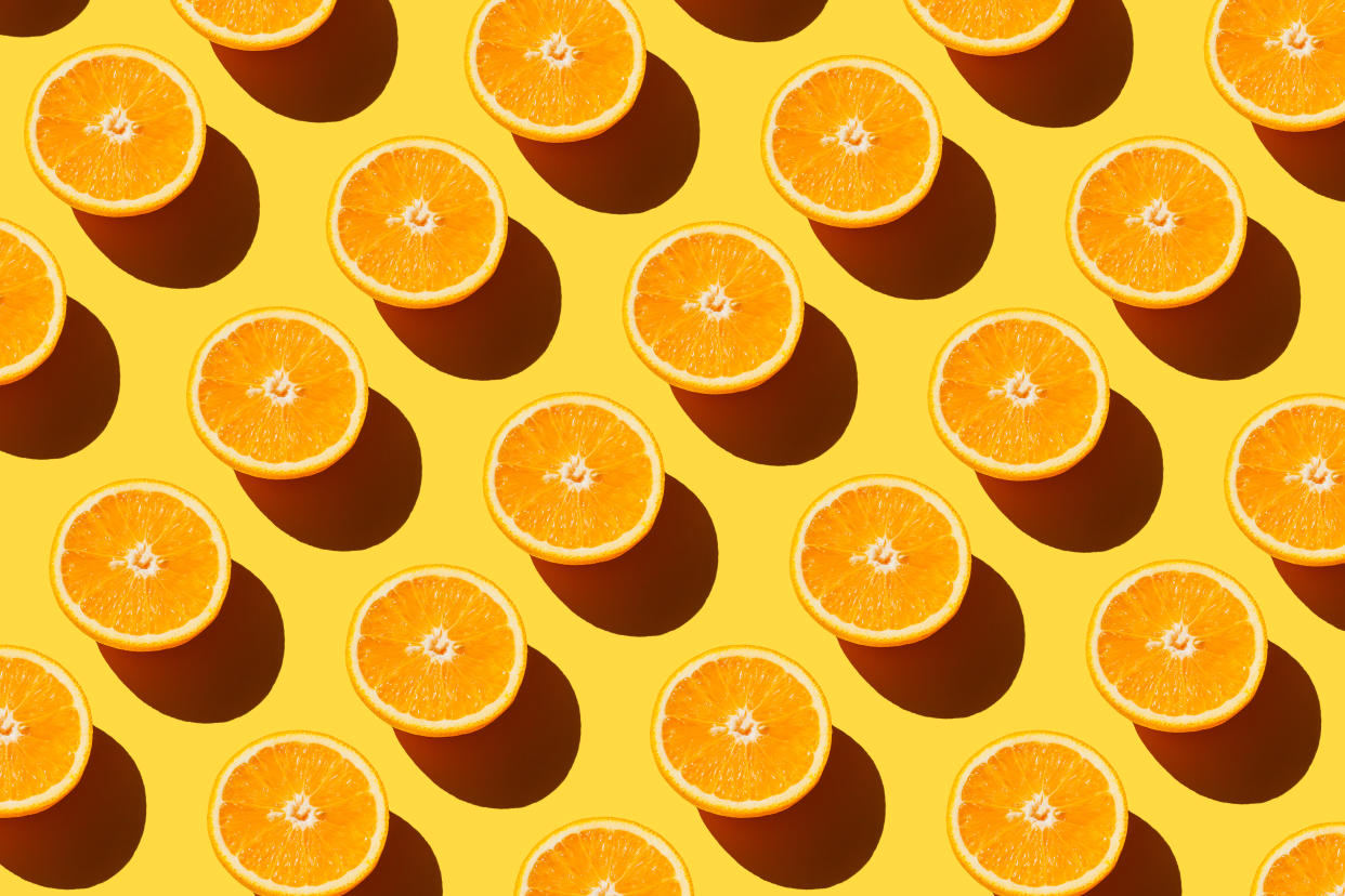 A number of cut oranges against a yellow background.