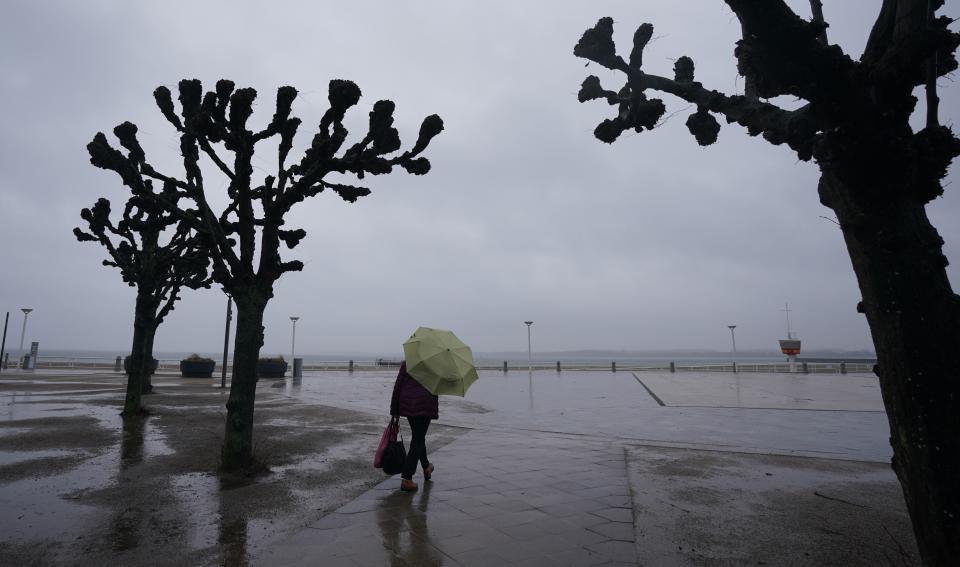 A passerby walks in the rain along the deserted promenade at the Baltic Sea in Travemuende, Germany, Friday, Feb. 18, 2022. (Marcus Brandt/dpa via AP)