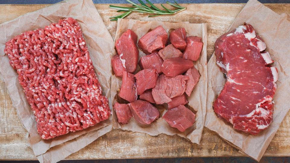 Fresh raw angus beef meat, whole, ground and chopped on parchment paper , wooden cutting board,  stone background, top view.