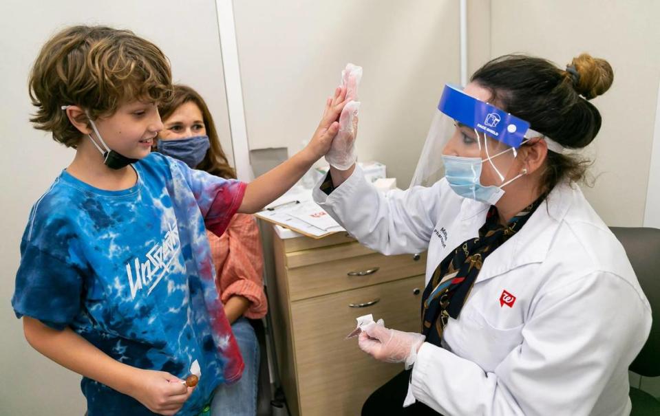 Leo Johnson, 8, high-fives pharmacist Maylen Mesa after receiving the Pfizer-BioNTech COVID-19 vaccine from Mesa at a Walgreens in Miami, Florida, on Saturday, Nov. 6, 2021. His masked mom, Allison Johnson, is in the background.