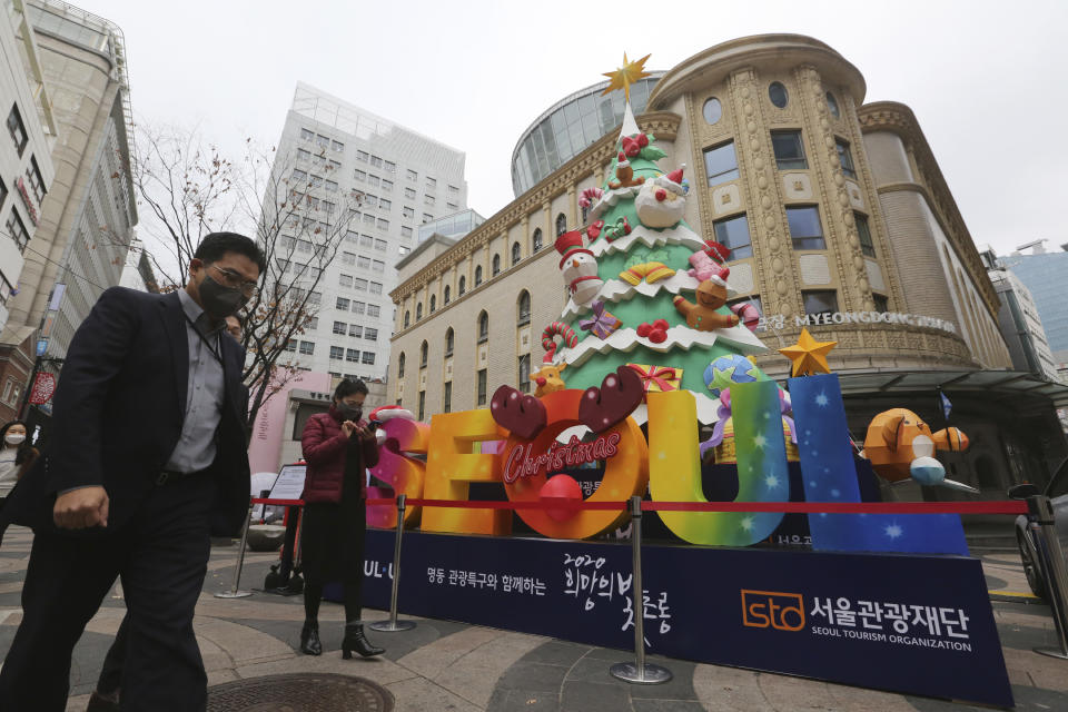 People wearing face masks to help protect against the spread of the coronavirus walk past a Christmas tree set up for a year-end festival featuring a lantern at a shopping street in Seoul, South Korea, Friday, Nov. 20, 2020. South Korea's prime minister has urged the public to avoid social gatherings and stay at home as much as possible as the country registered more than 300 new virus cases for a third consecutive day. (AP Photo/Ahn Young-joon)