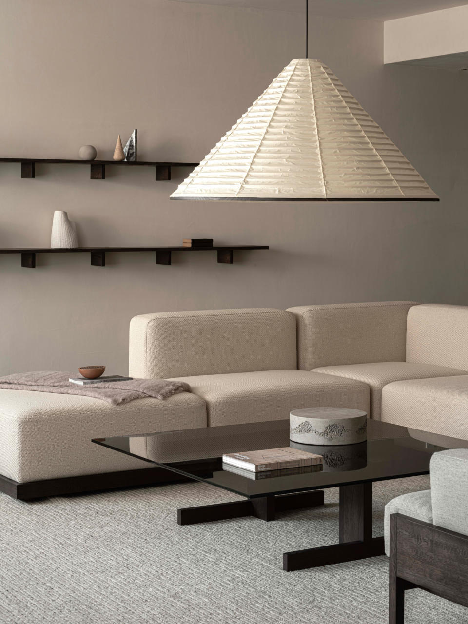 A warm beige living room with beige modular sofa, black gloss coffee table and oversized paper lantern