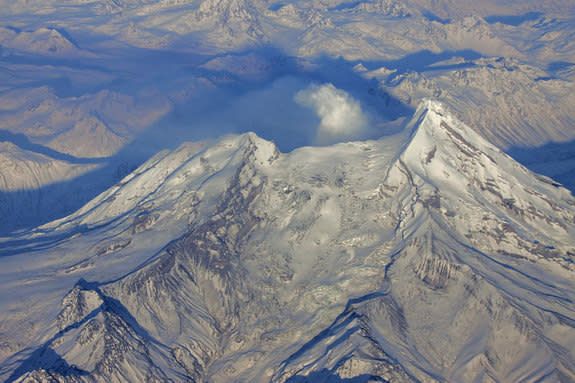 Alaska's Redoubt volcano during its 2009 eruption, with ash visible against the new snow and a cloud of volcanic gas and steam drifting to the northn.