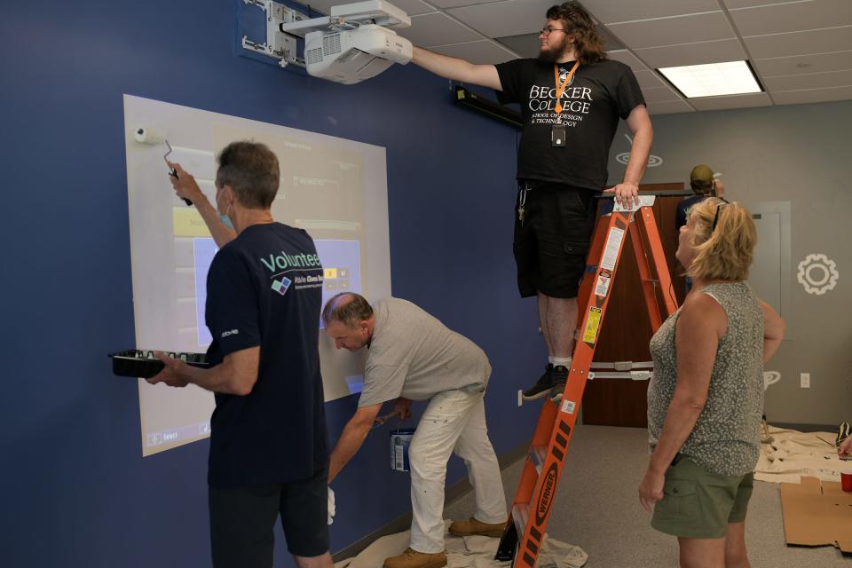 On ladder WPS IT department employee Cory Cooper works to hook up an EPSON projector for the STEM lab as volunteers paint with WPS IT department employee Dianna Leduc, at right.  About 150 AbbVie volunteers from the Worcester facility showed up at Forest Grove Middle School to work on a greenhouse and enhance the STEM lab. The group was volunteering to help develop an immersive, large-scale STEM lab on the school’s campus Wednesday.