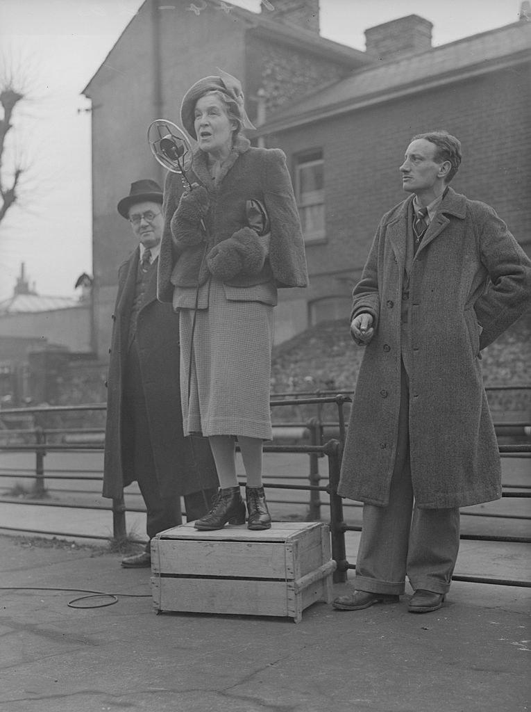 A woman stands on a soapbox and speaks into a microphone