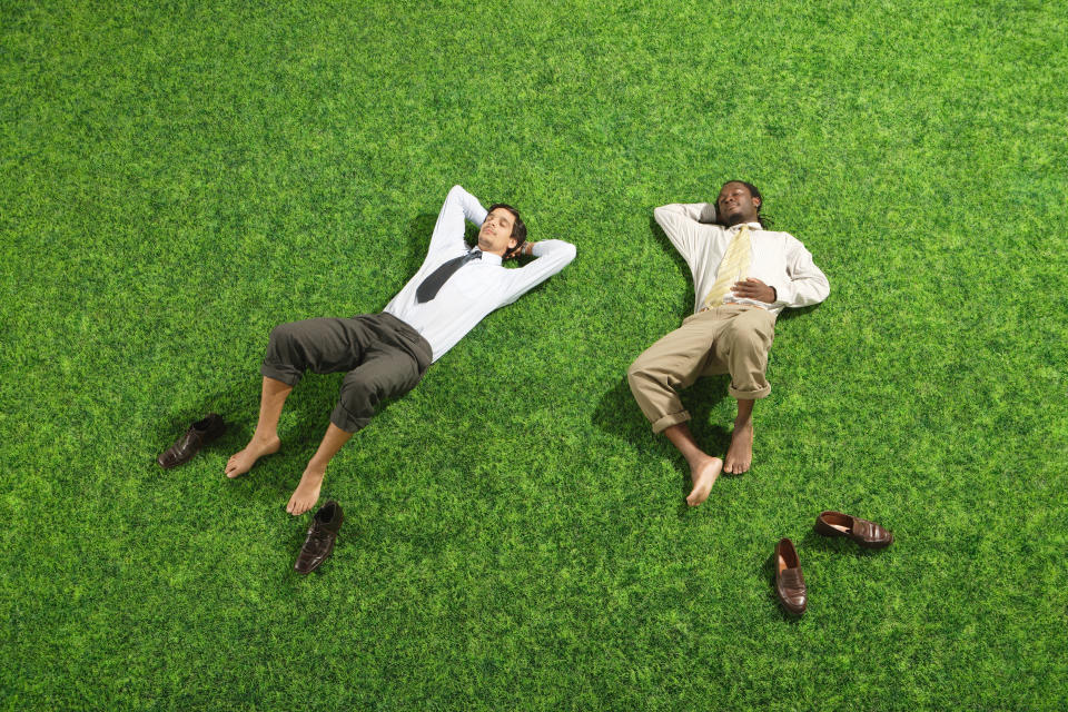 two office workers lying on the grass with their shoes off