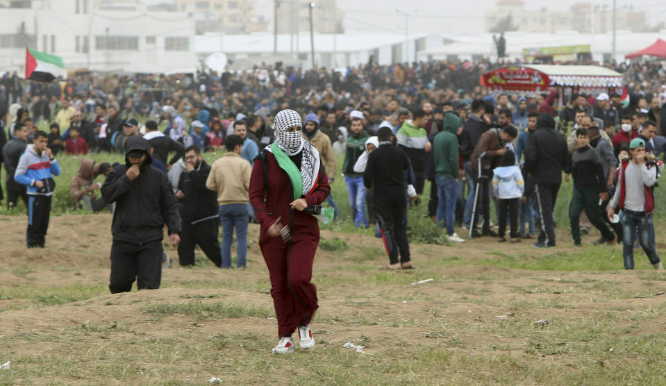 A protestor woman walks toward the Gaza Strip's border with Israel, while others gather to mark first anniversary of Gaza border protests east of Gaza City, Saturday, March 30, 2019. Tens of thousands of Palestinians on Saturday gathered at rallying points near the Israeli border to mark the first anniversary of weekly protests in the Gaza Strip, as Israeli troops fired tear gas and opened fire at small crowds of activists who approached the border fence. (AP Photo/Adel Hana)