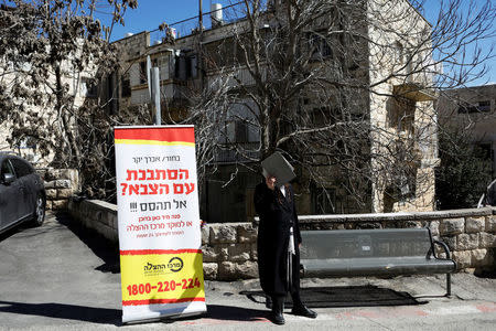 An Ultra-Orthodox Jewish man covers his face as he stands near a banner, in front of the Israeli military recruiting office in Jerusalem, March 13, 2018. REUTERS/Ronen Zvulun