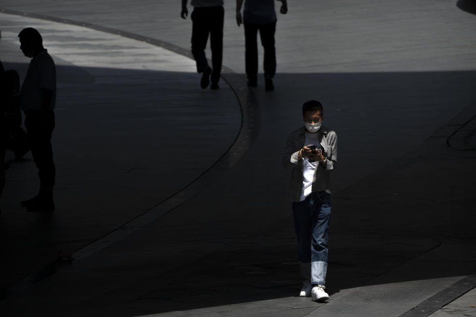 A man wearing a face mask walks through a shopping and office complex in Beijing, Thursday, June 30, 2022. (AP Photo/Mark Schiefelbein)