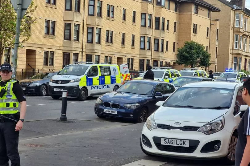 Two armed police officers on Kenmure Street, with four police vehicles.