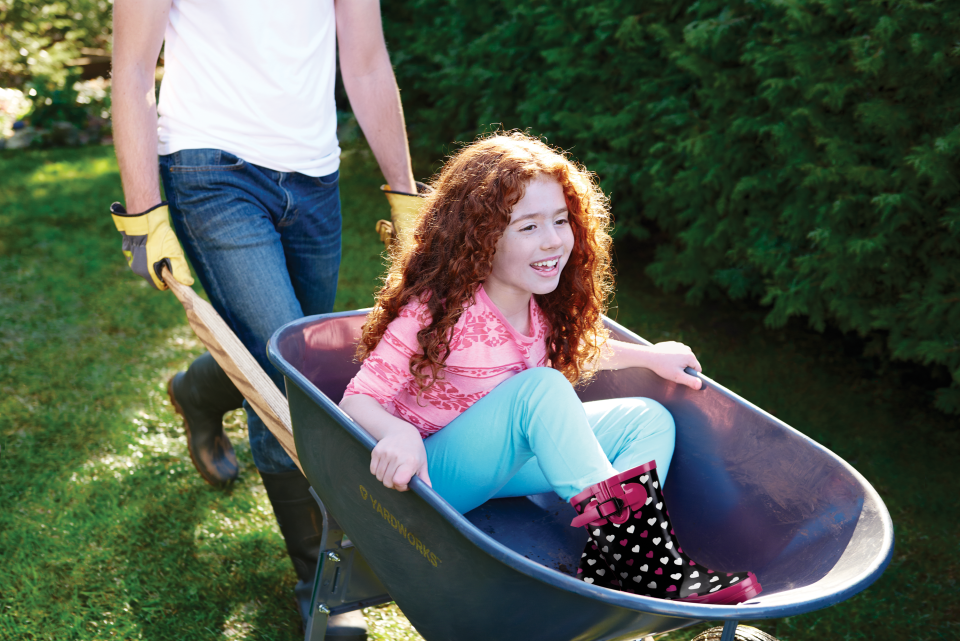 Photo of a person pushing their child in a wheelbarrow on the lawn