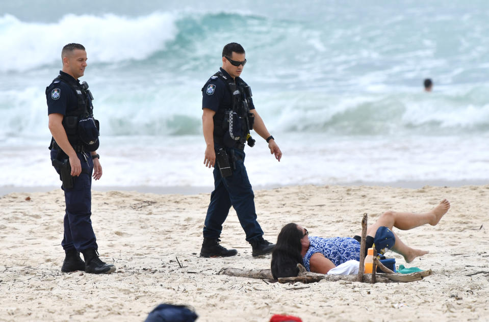 Picture shows two Queensland Police officers appearing to tell a sunbather to move along at Burleigh Beach on the Gold Coast