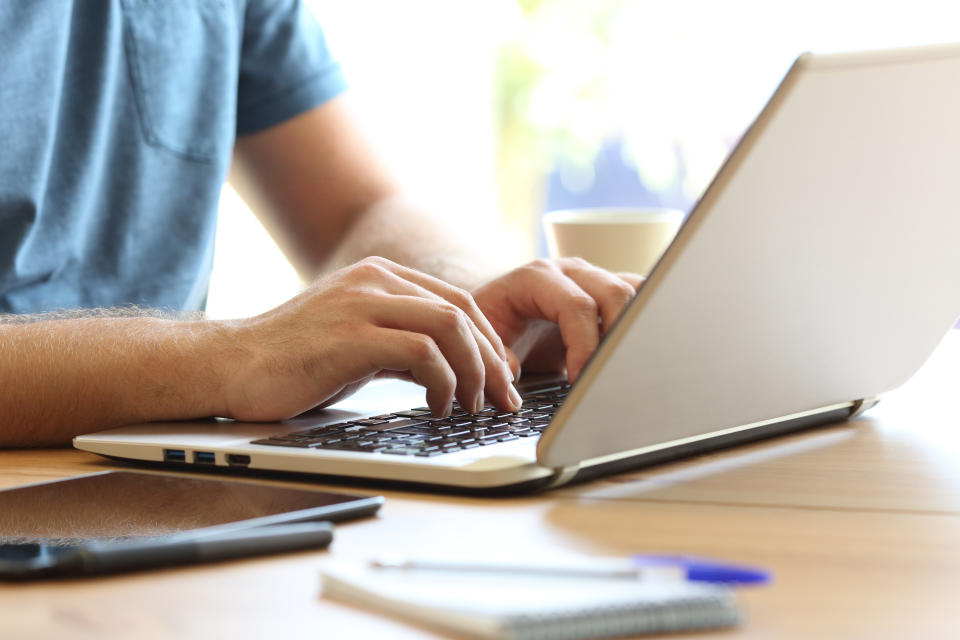 Close up of man hands typing on a laptop keyboard on a desk at home or office