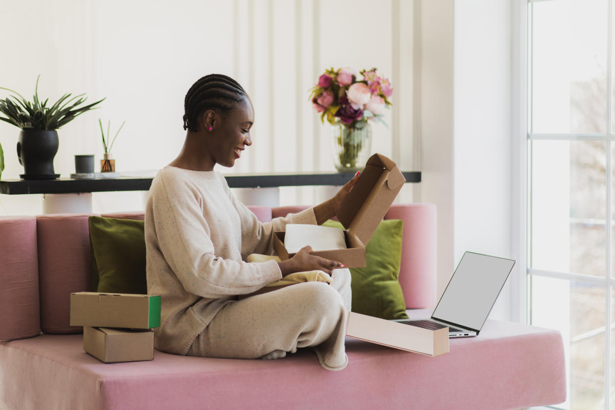 Cheerful afro-american woman receiving long awaited delivery, getting online order indoors. Satisfied female customer receiving her good internet purchase in cardboard package in living room interior. Online store and purchase delivery. Copy space. Fast dilivery service.