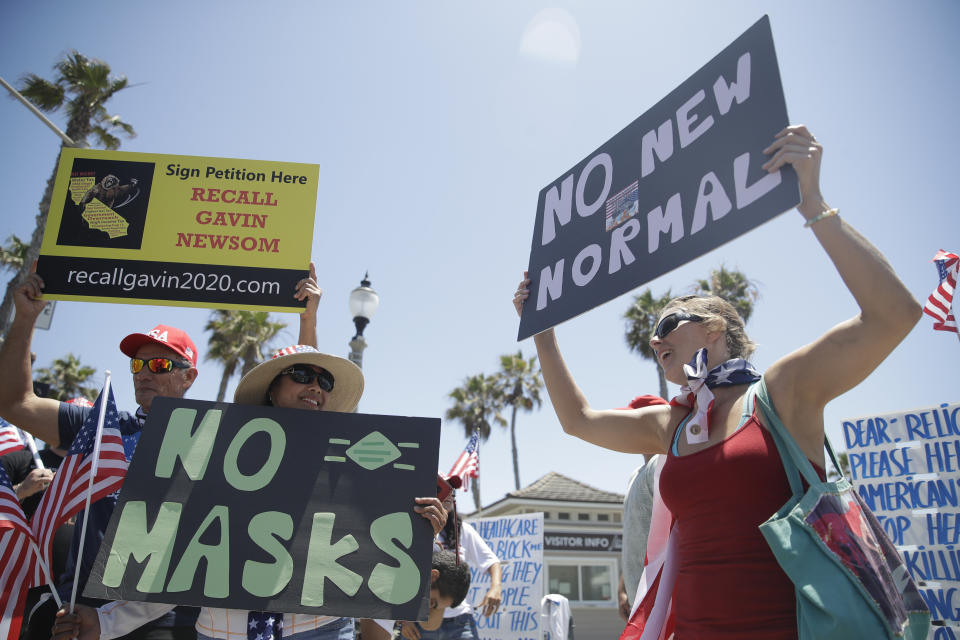 Demonstrators hold signs as they protest the lockdown and wearing masks Saturday, June 27, 2020, in Huntington Beach, Calif. (AP Photo/Marcio Jose Sanchez)