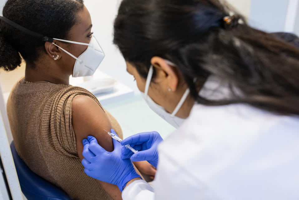 Dr. Grace Lam said the COVID-19 vaccine is one of the best things people can do to avoid developing long COVID. (Image via Getty) Medical clinic view of a woman being vaccinated by a woman doctor of indian ethnicity