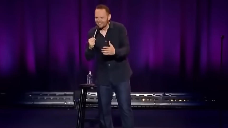 Bill Burr in a black shirt and holding a microphone on stage