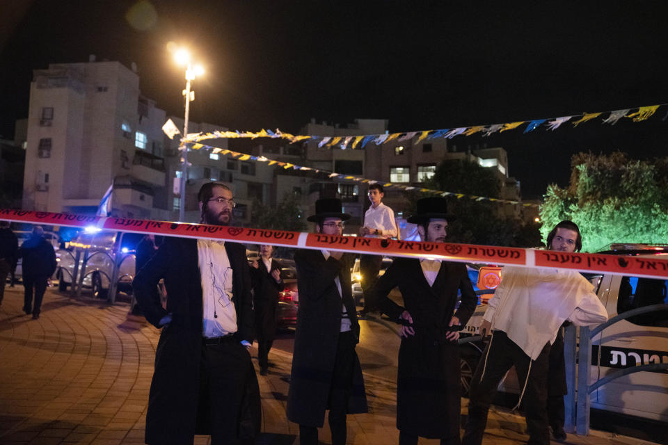 Ultra-Orthodox Jews stand behind police tape after a stabbing attack in the town of Elad, Israel, Thursday, May 5, 2022. Israeli medics say at least three people were killed in a stabbing attack near Tel Aviv on Thursday night. Israeli police said they suspect it was a militant attack. (AP Photo/Maya Alleruzzo)