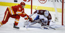 Colorado Avalanche goalie Darcy Kuemper, right, covers the puck as Calgary Flames' Mikael Backlund reaches for it during the second period of an NHL hockey game Tuesday, March 29, 2022 in Calgary, Alberta. (Jeff McIntosh/The Canadian Press via AP)