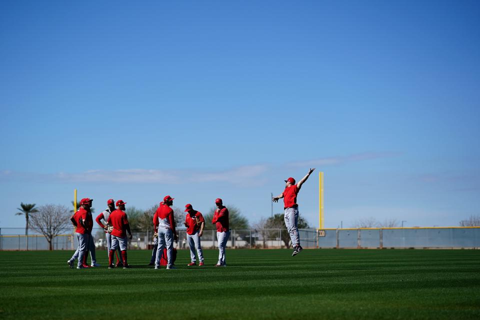Coach Collin Cowgill jumps to demonstrate a technique while working with the Reds  outfielders before the games began.