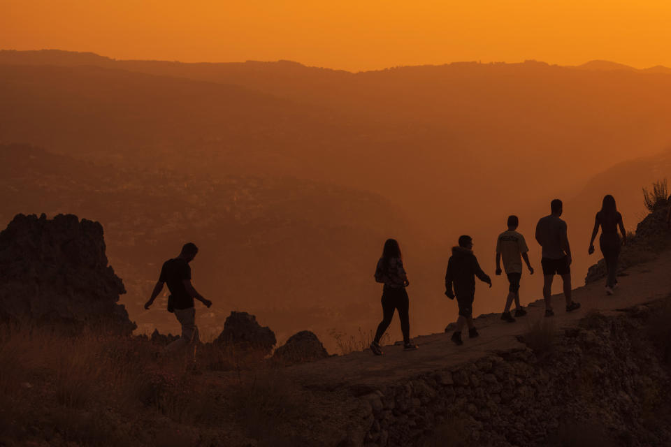 Hikers walk along a cliff to see the sunset over the scenic Kadisha Valley, a holy site for Lebanon's Maronite Christians, in the northeast mountain town of Bcharre, Lebanon, Friday, July 21, 2023. For Lebanon's Christians, the cedars are sacred, these tough evergreen trees that survive the mountain's harsh snowy winters. They point out with pride that Lebanon's cedars are mentioned 103 times in the Bible. (AP Photo/Hassan Ammar)