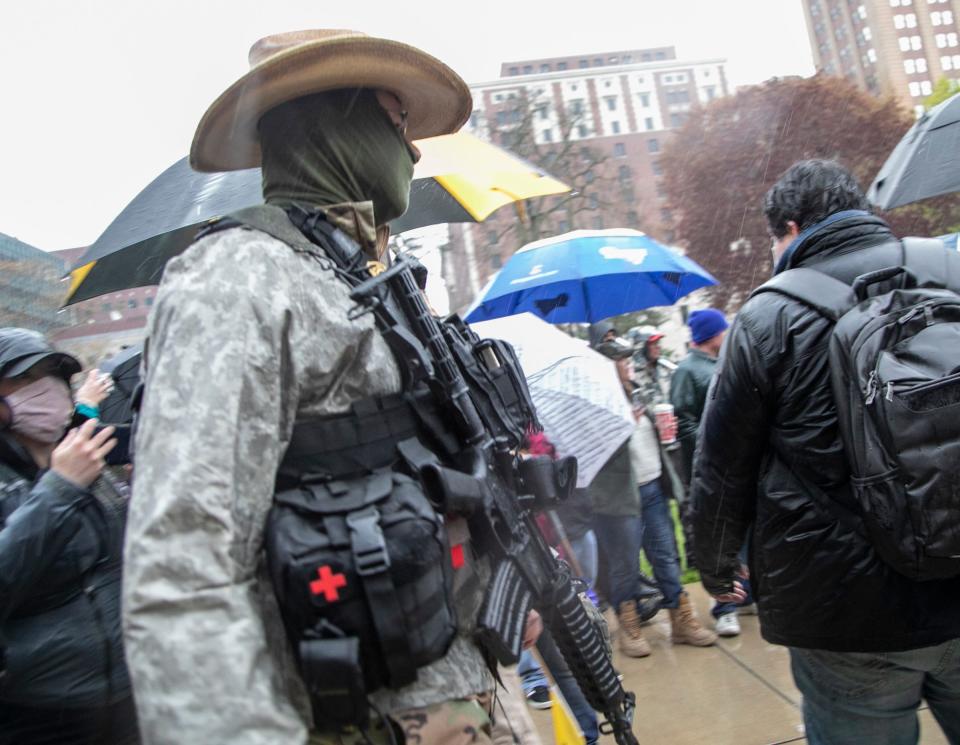 A man carrying an gun hurries to watch Michigan State Police surround a man involved in a scuffle as protestors gather in the pouring rain outside of the Michigan State Capitol in Lansing Thursday, May 14, 2020, to protest Governor Whitmer's stay in place mandate. 