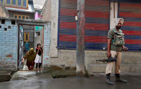 A girl peers from her house as a member of the security forces patrols a street in Srinagar as the city remains under curfew following weeks of violence in Kashmir August 19, 2016. REUTERS/Cathal McNaughton