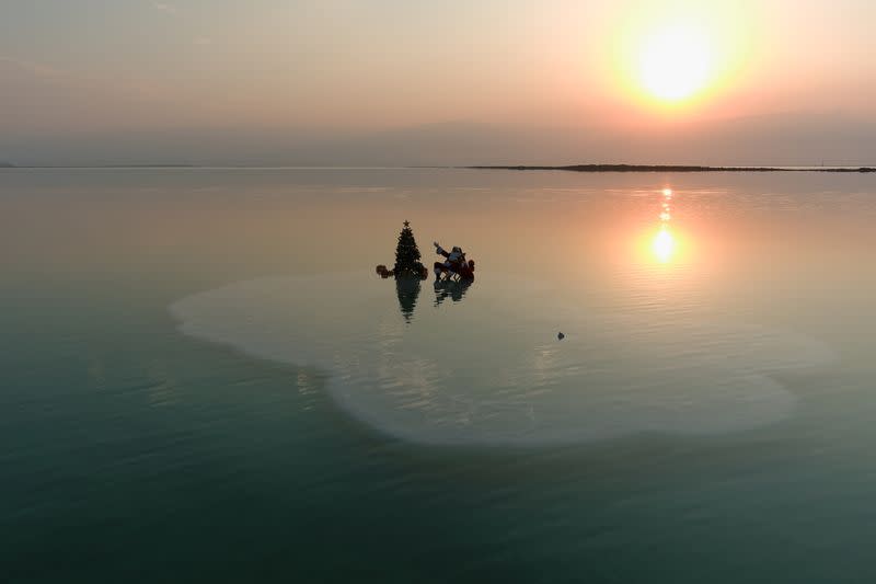 Issa Kassissieh, wearing a Santa Claus costume, gestures as he sits next to a Christmas tree while posing for a picture on a salt formation in the Dead Sea, near Ein Bokeq