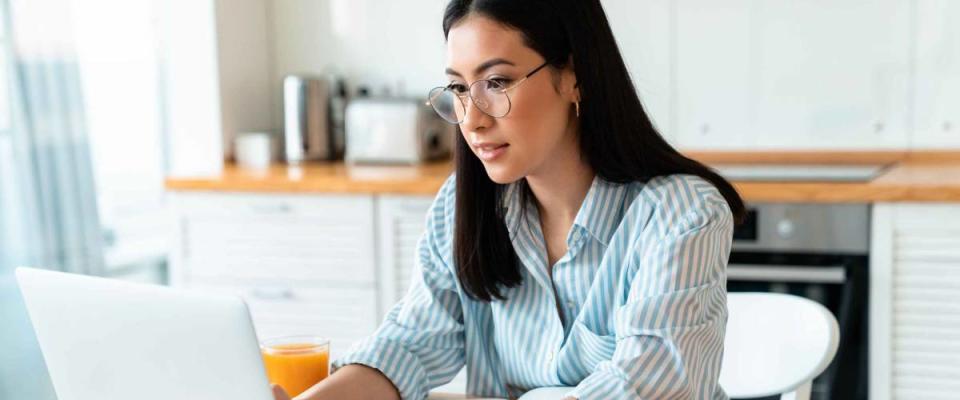 Image of a beautiful concentrated brunette young woman at the kitchen indoors at home using laptop computer work.