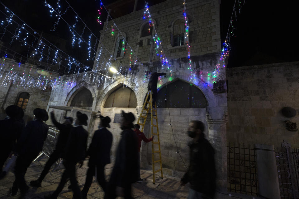 Jewish men walk past Palestinian men stringing colored lights across a main walkway on the eve of the Muslim holy month of Ramadan in the Old City of Jerusalem, Monday, April 12, 2021. (AP Photo/Maya Alleruzzo)