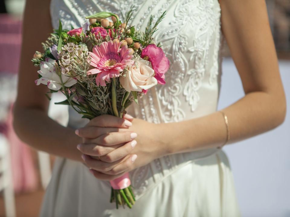 Bride in white dressing holding pink and green flower bouquet with both hands