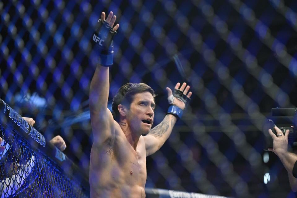 A shirtless man raising his arms inside a fighting ring