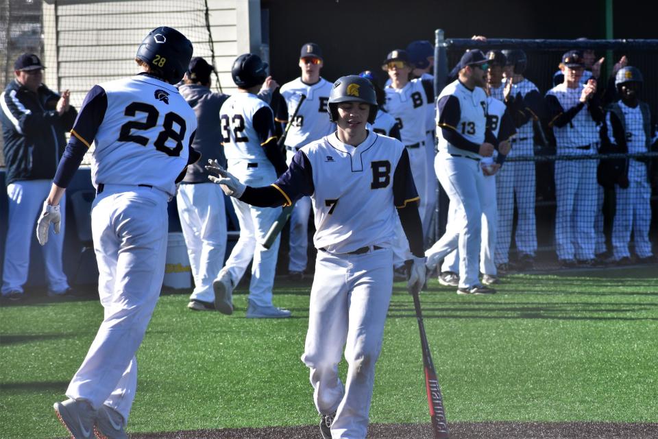 Battle's Donovan Hicks (7) high-fives Josh Candrl (28) after Candrl scored a run during the Spartans' 4-1 loss to Park Hill South on March 25 at Battle High School.