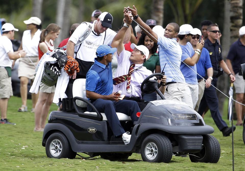 A spectator lifts up a rope as Tiger Woods, left, rides in a cart with his caddy Joe LaCava, center, after play was suspended due to approaching inclement weather during the first round of the Cadillac Championship golf tournament, Thursday, March 6, 2014, in Doral, Fla. (AP Photo/Lynne Sladky)