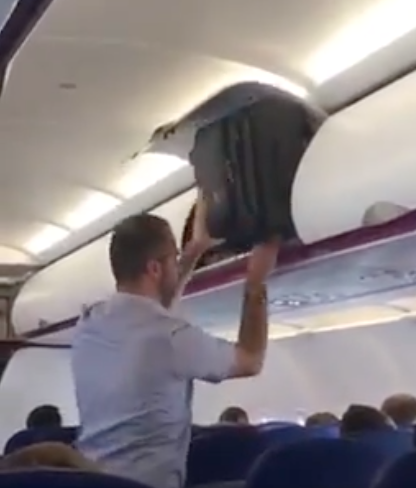 A man has been filmed trying to shove his bag into the overhead bin on a plane. Photo: Twitter/@lazblue/jukin media