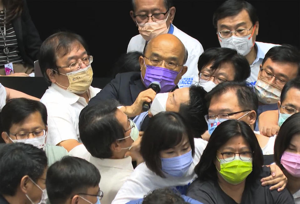 In this image taken from video by Taiwan's EBC, Premier Su Tseng-chang, in purple mask, tries to make a policy speech amid a scuffle between opposition Nationalist party and ruling Democratic Progressive Party lawmakersduring a parliament session in Taipei, Taiwan, Tuesday, Sept. 28, 2021. Taiwan's legislature on Tuesday descended into a rowdy brawl on Tuesday, after opposition lawmakers interrupted an important policy address and rushed the podium. (EBC via AP )