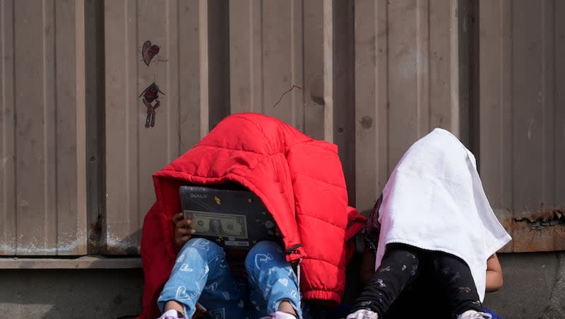 Children cover their heads as they sit outside of a migrant shelter Wednesday, March 13, 2024, in the Pilsen neighborhood of Chicago. Multiple people living at the shelter for migrants have tested positive for measles since last week. A team from the Centers for Disease Control and Prevention is supporting local officials' response.