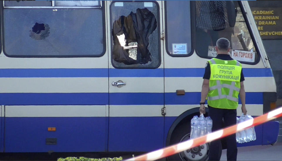 A policeman brings water for hostages contained in a bus after an armed man seized the long-distance bus and took some 10 people hostage in the city centre of Lutsk, some 400 kilometers (250 miles) west of Kyiv, Ukraine on Tuesday July 21, 2020. The assailant is armed and carrying explosives, according to a Facebook statement by Ukrainian police. Police officers are trying to get in touch with the man and they have sealed off the area. (Ukrainian Police Press Office via AP)