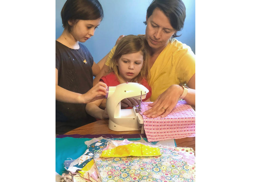 This April 3, 2020 photo shows Erin Bried, right, with her daughters Ellie, 9, left, and Bea, 4, as they sew masks. Bried is the author of "How to Sew a Button: And Other Nifty Things Your Grandmother Knew," left, and "How to Build a Fire: And Other Handy Things Your Grandfather Knew," (Holly Bemiss via AP)