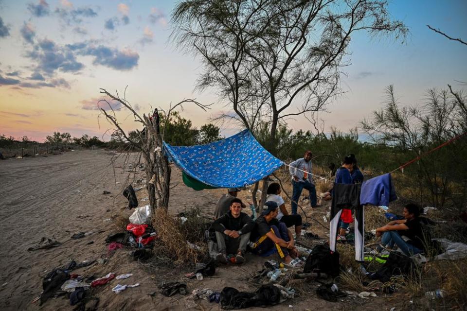 A group of people rest under a makeshift shelter in the desert.