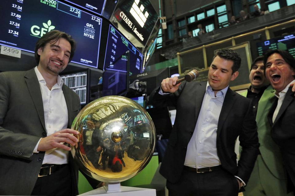 GFL Environmental Founder, President & CEO Patrick Dovigi, second left, is joined by BC Partners Paolo Notarnicola, left, as he rings a ceremonial bell on the floor of the New York Stock Exchange, celebrating his company's IPO, Wednesday, March 4, 2020. (AP Photo/Richard Drew)