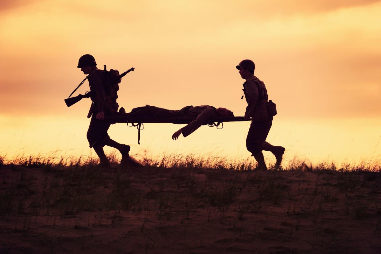 Silhouette of two WWII Army Soldiers/Medics carrying a wounded soldier on a stretcher to safety and help.