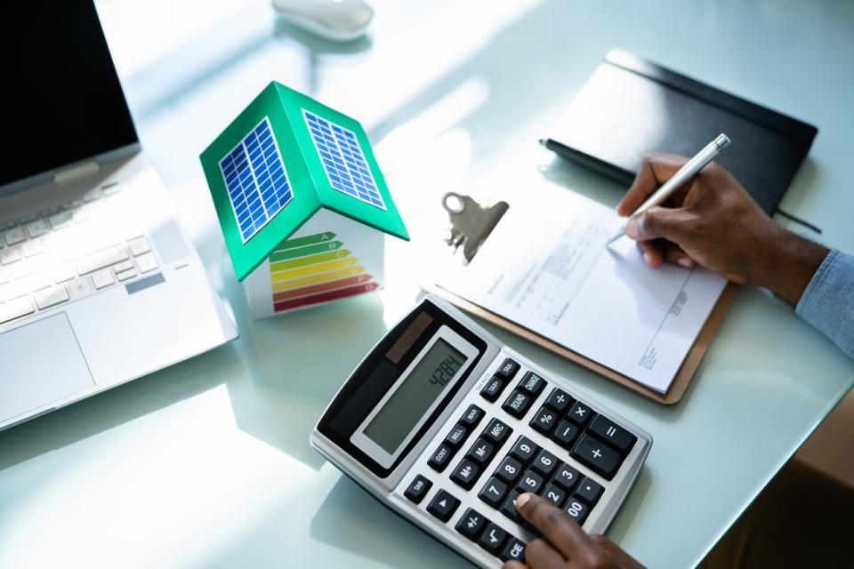 overhead view of desktop with calculator and clipboard with graph and small model of energy efficient home energy audit concept