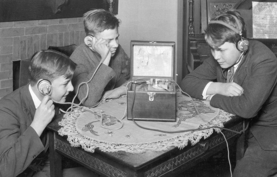 <p>A group of young boys gather around the table to listen to the radio. The 1920s saw a huge boom in consumer radios, which were still a relatively new invention.</p>