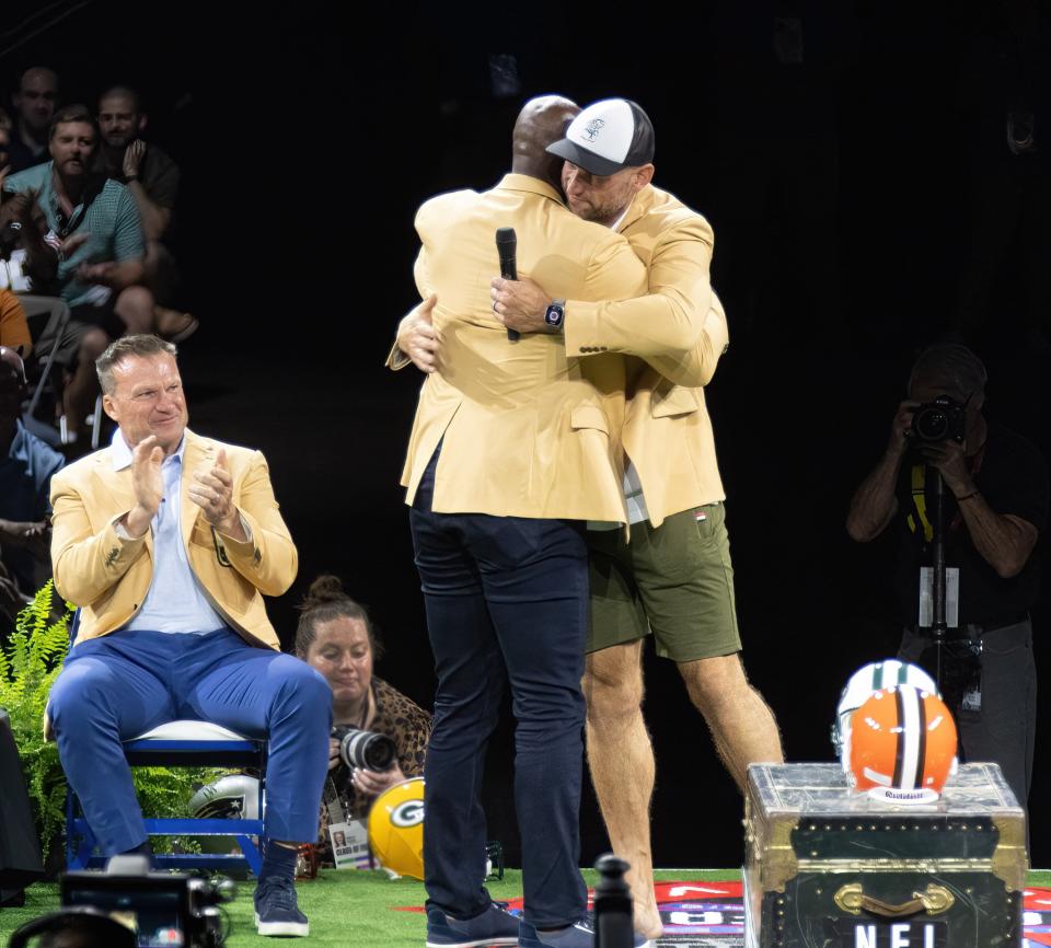New Hall of Famers DeMarcus Ware and Joe Thomas (in shorts) hug Sunday in front of an applauding Zach Thomas during the Enshrinees’ Roundtable.