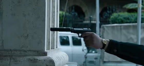 A hitman pointing a gun with a silencer at Maurizio (off-screen) in "House of Gucci"