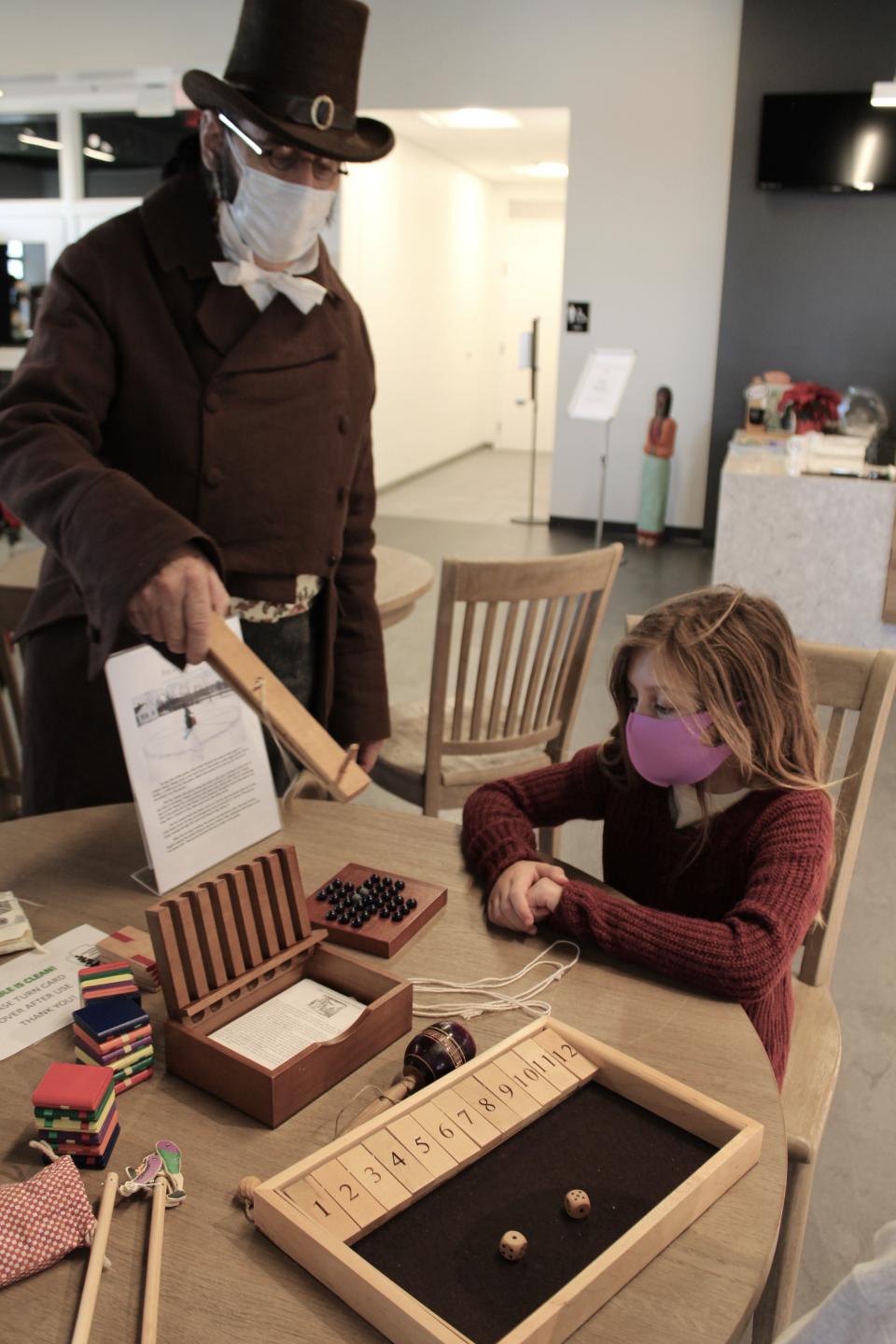 Ken Roberts of St. Clair Shores (left) shows Kendyl Lee, 6, of Monroe a version of French bilboquet, a ball and cup game.