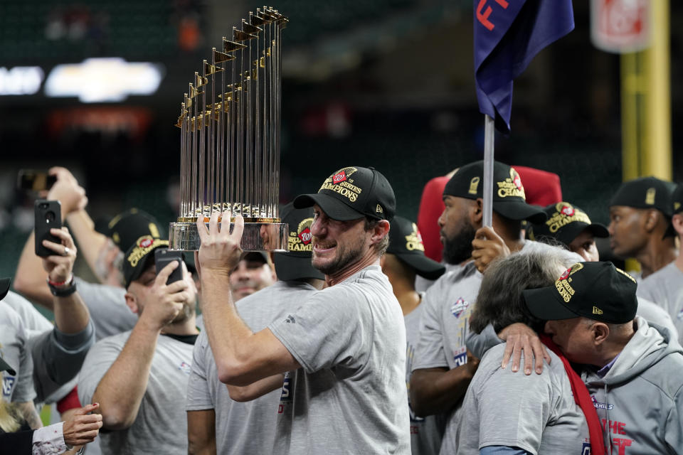 FILE - In this Oct. 30, 2019, file photo, Washington Nationals starting pitcher Max Scherzer celebrates with the trophy after Game 7 of the baseball World Series against the Houston Astros in Houston. The Nationals head to spring training with mostly the same squad that won the World Series. They are counting again on being led by a star-studded rotation featuring Scherzer and Stephen Strasburg, along with slugger Juan Soto. (AP Photo/David J. Phillip, File)